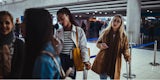 Two young people looking at their phones while they wait in line to check-in at the airport.