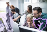 A group of workers collaborating and looking at a set of computer terminals.